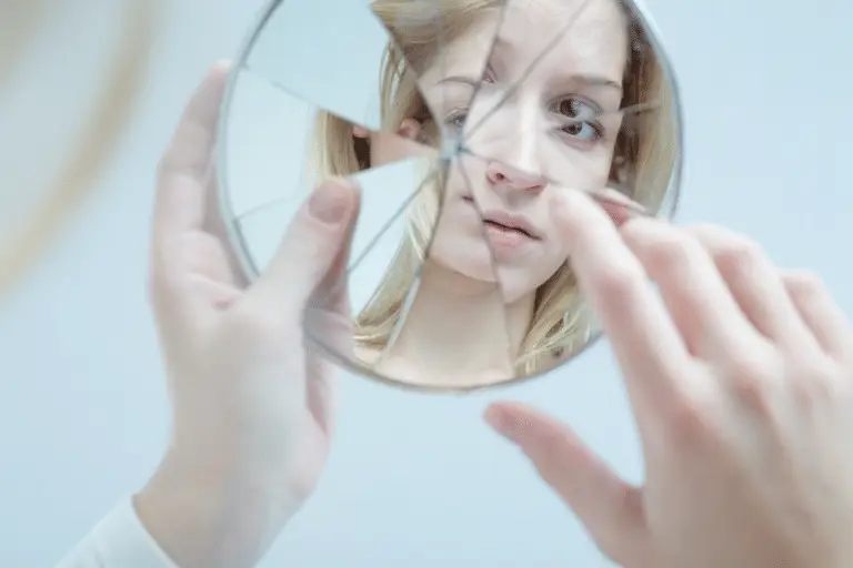 woman touching her reflection in broken mirror What no one tells you about body dysmorphic disorder . Makin Wellness . online body dysmorphia therapy