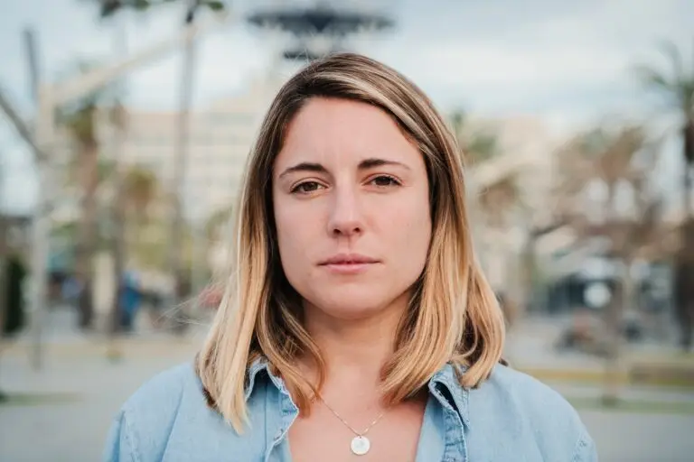 A young blonde woman staring into the camera as she works through her difficult feelings.