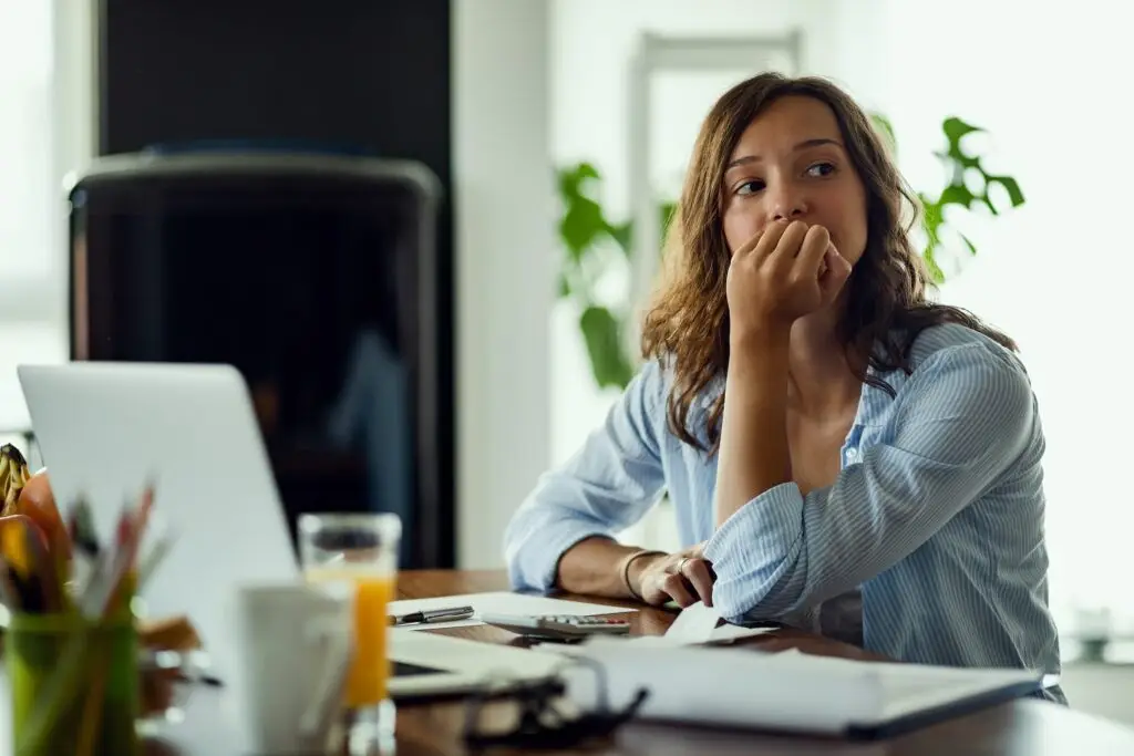 woman sitting at her desk trying to do her work but feels stressed and distracted, so she is holding her head up with her fist under her chin and looking off into the distance to think