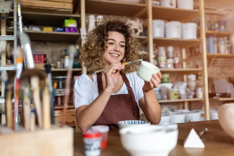 A young woman painting glaze on a piece of pottery.