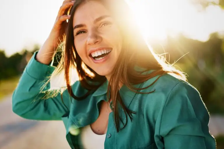 A young woman smiling and laughing while the sun is beaming behind her.