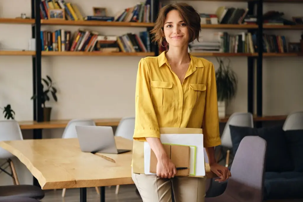 A young woman confidently standing with work papers.