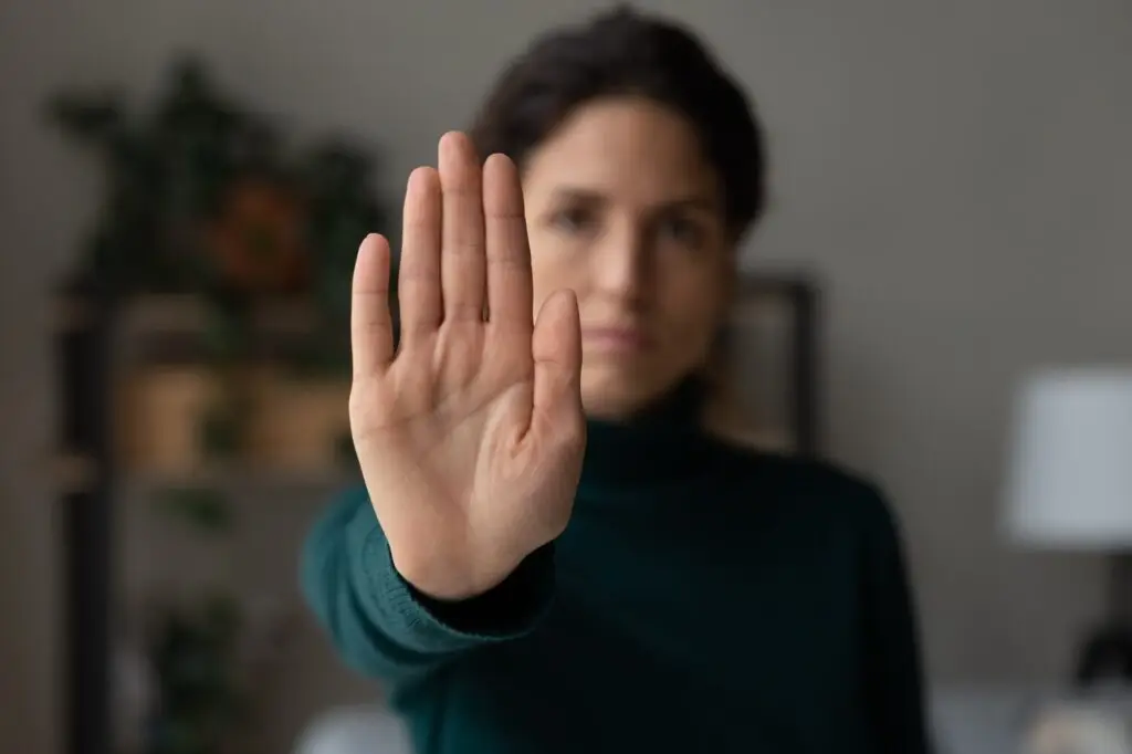 A woman standing with her palm outwardly stretched to near the front of the camera to signify a boundary she is expressing.