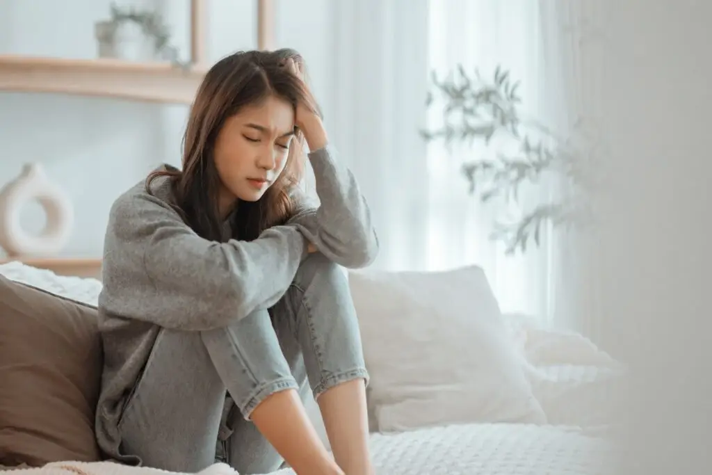 A young woman holding her knees to her chest, holding her head in her hands as she feels distress from her Cptsd symptoms.