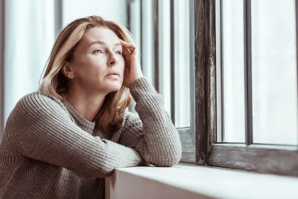 A woman looking out of a window on a bright day while she processes her abusive relationship.