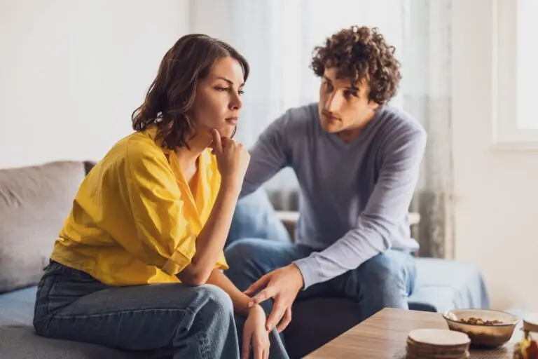 A young white couple having a difficult conversation on a couch.