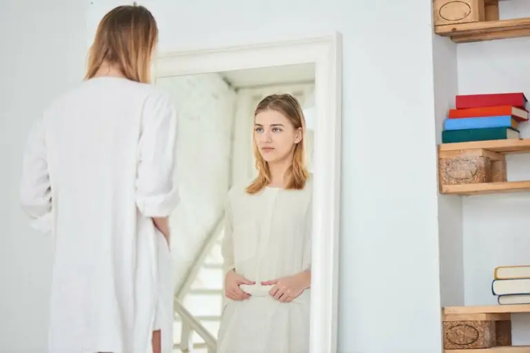 A young woman examining herself in her mirror, unhappy with what she sees.