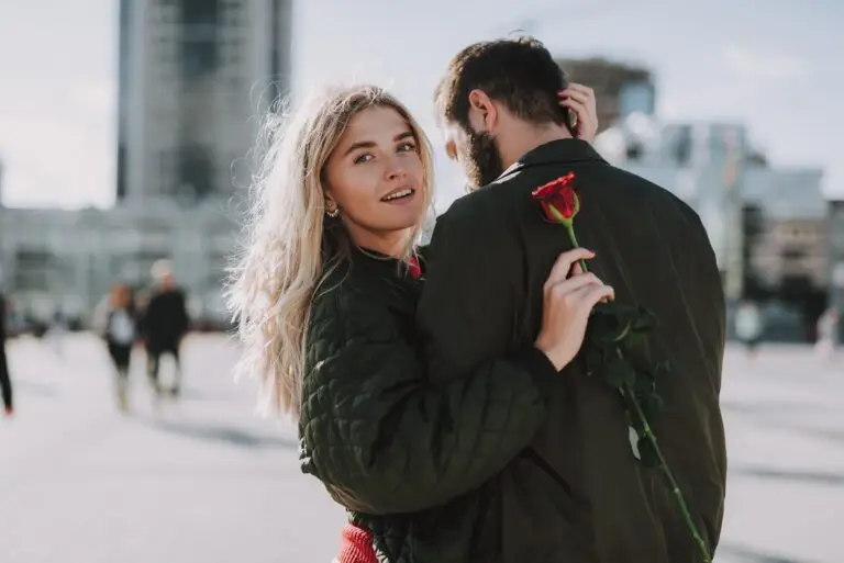 A young woman embracing her significant other while holding a rose behind his back.