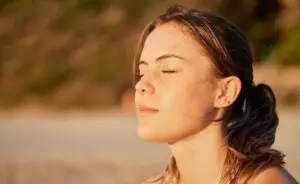 A woman sitting in the outdoors with her eyes closed as the sun hits her face.