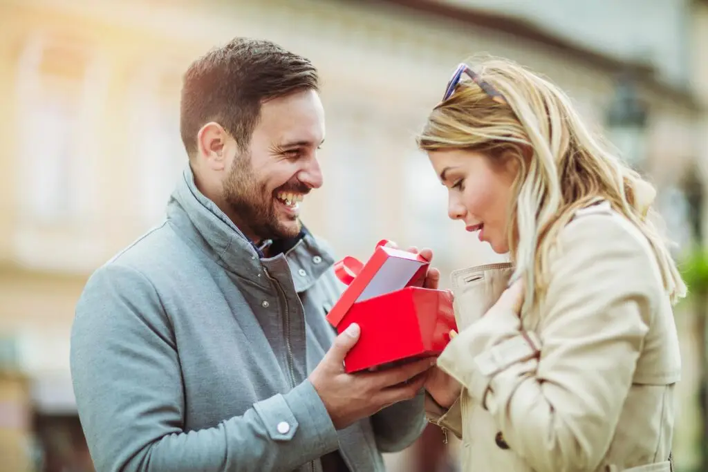 A man giving his girlfriend a surprise gift. She is shocked as he opens it.