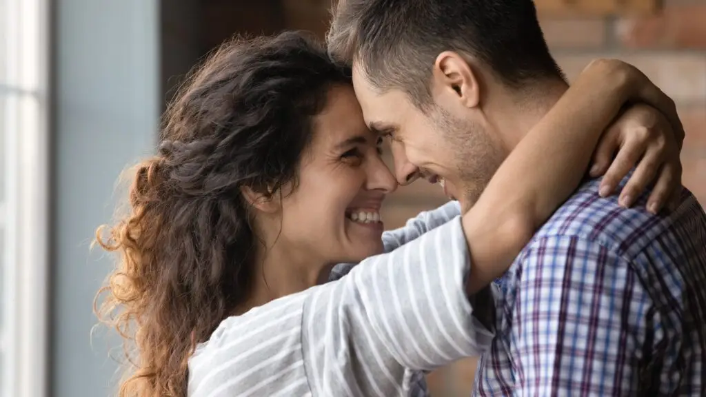 A happy, smiling couple hugging while touching foreheads and looking into each other's eyes showing what real love looks like.