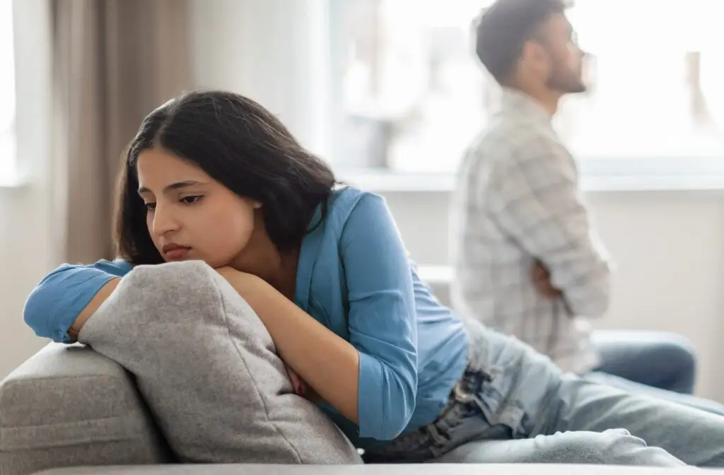 A woman stressed out, turned away from her husband, who's body language is showing he's upset at her.