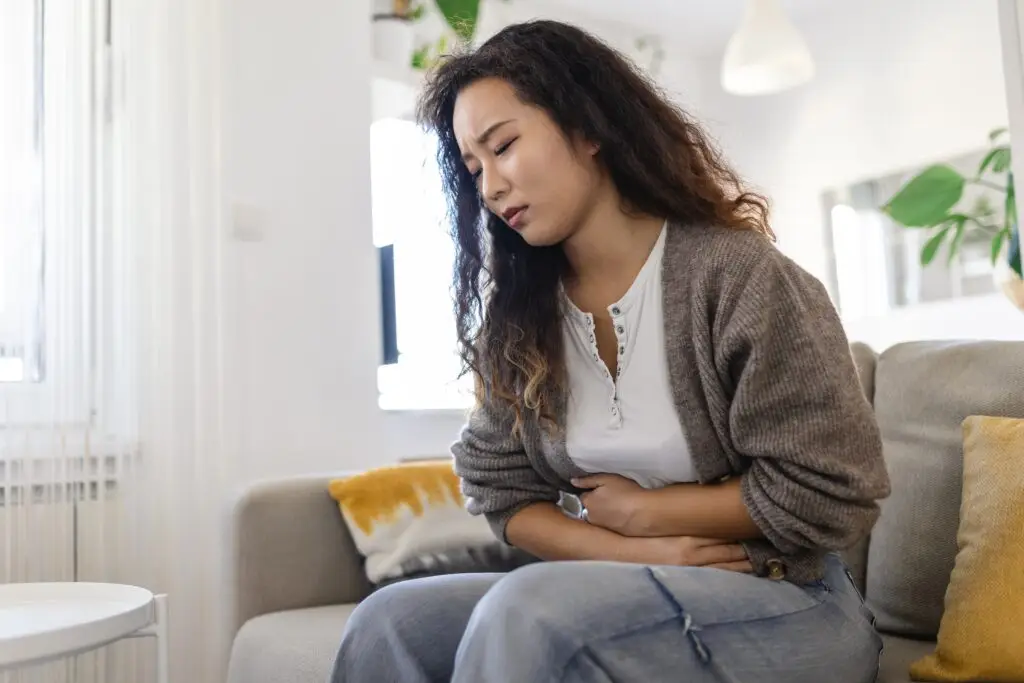 A woman sitting on her couch holding her stomach looking in pain from a binge eating episode.