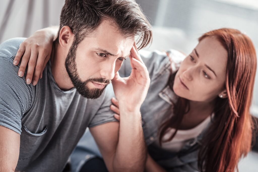 a man holding his head in his hand, manipulating the situation, while a woman is trying to comfort him.