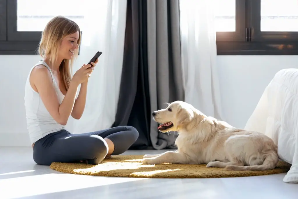 A young woman sitting on her bedroom floor cross-legged with her dog, texting friends while she learns to use coping strategies for managing her depression over college summer break