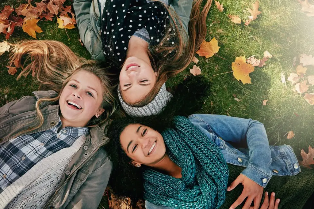 group of teenage girls laying on the ground with their heads close together, looking up and smiling as they have a good time together