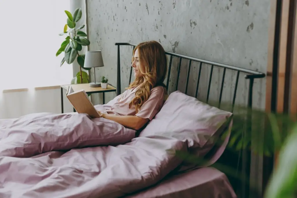 Young woman sitting up in bed reading to help improve her sleep despite her ADHD