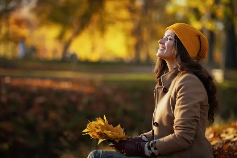 A middle-aged woman sitting on a park bench with fall leaves in her hand, thinking about how to move on after a divorce.