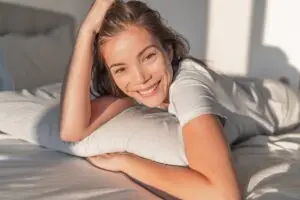 young woman perched over her pillow, waking up to the sun shining through her window, smiling because she got a great night sleep despite her adhd