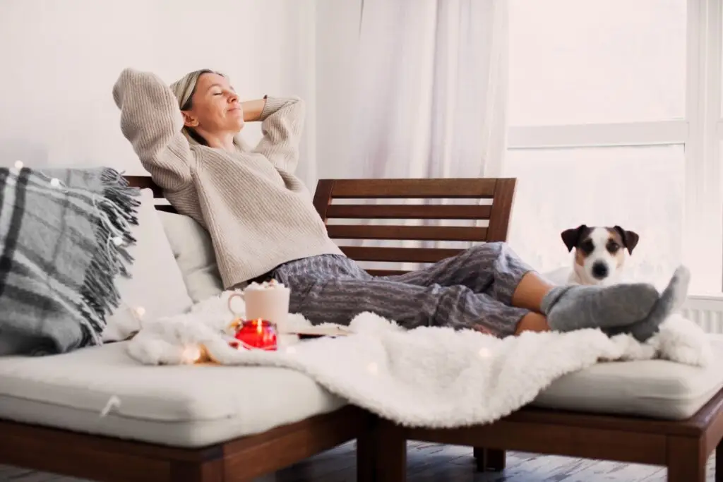 Middle aged woman relaxing on her couch, with her dog, soft blanket, and comfy pillows to practice self-care after a divorce