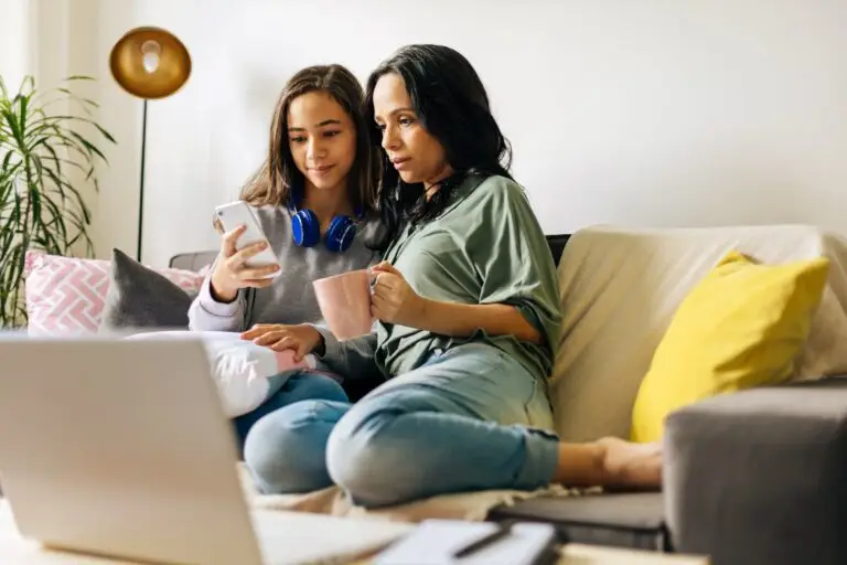 mother and teenage daughter looking hopeful while sitting on their couch, talking with the teenagers online therapist about peer pressure she experiences at school.