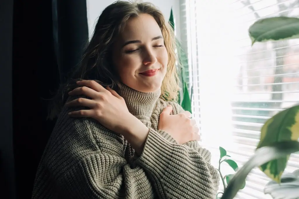 a young woman soothes herself by giving herself a hug as she cops with the grief of soon losing a loved one