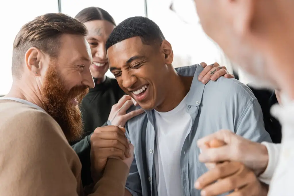 a group of men smiling and patting the back of one friend because he was able to open up and share how he feels about issues in his life.