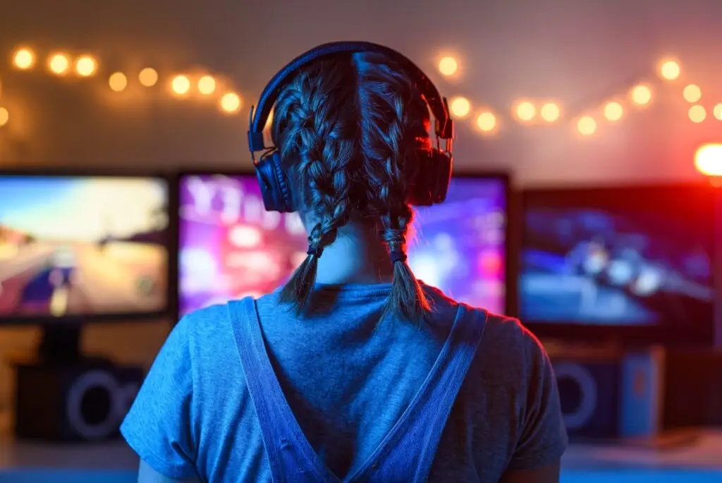 A girl plays video games at a computer. on the background of three monitors.