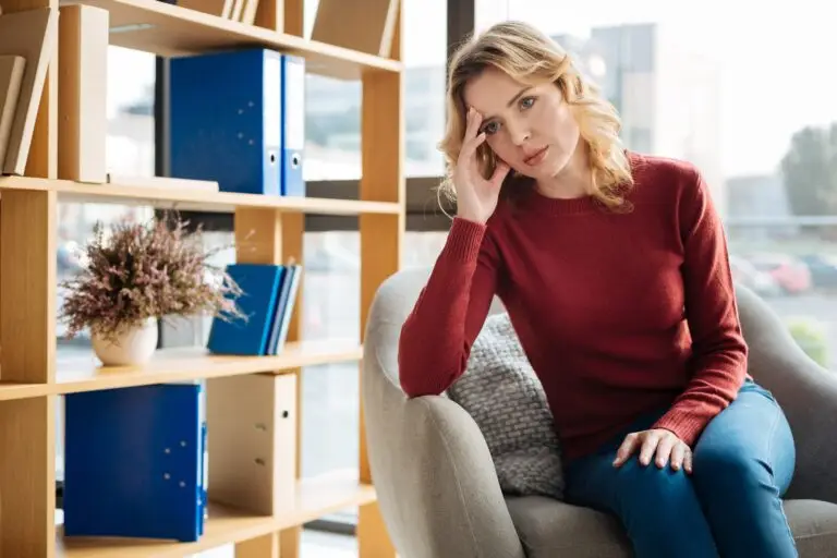 middle-aged blonde woman sitting in a chair with her hand holding her head up, concerned about the current state of the job market