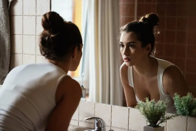 Young woman looking into the mirror as she tries to complete her hygiene routine, but is struggling to find the motivation.