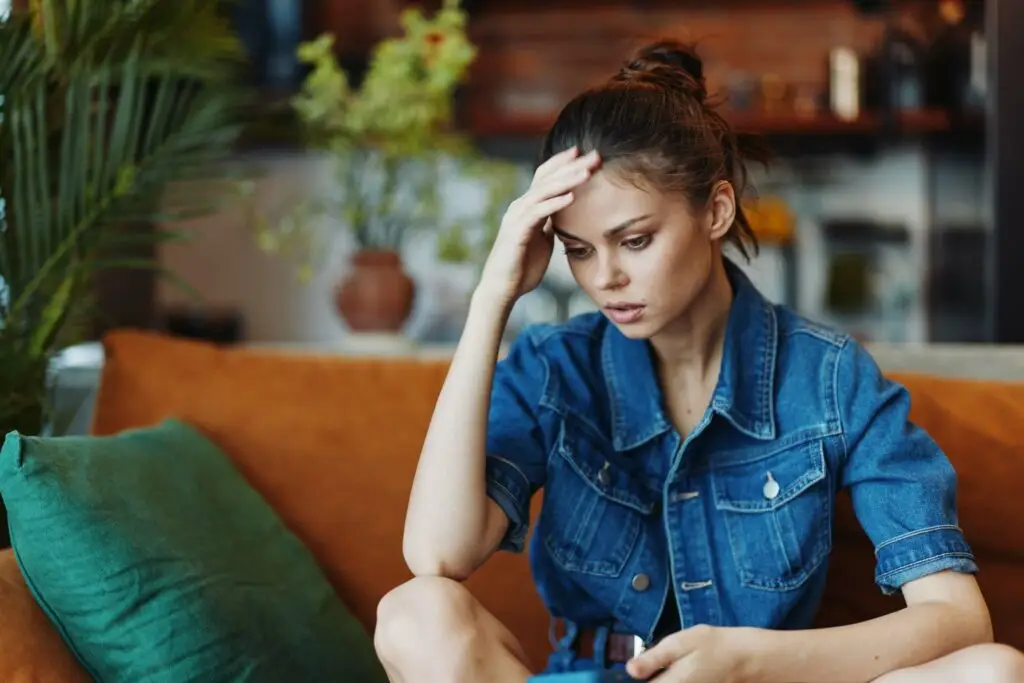 Young woman in a denim buttoned-up top feeling stressed, resting her hand on her forehead in frustration over her Combination type adhd (adhd-c) symptoms.