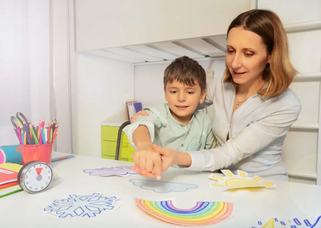 A mother is helping her young son point to different drawings on the table. The young boy has autism and requires some extra help with learning and communication, as he requires Level 2 support for his autism.