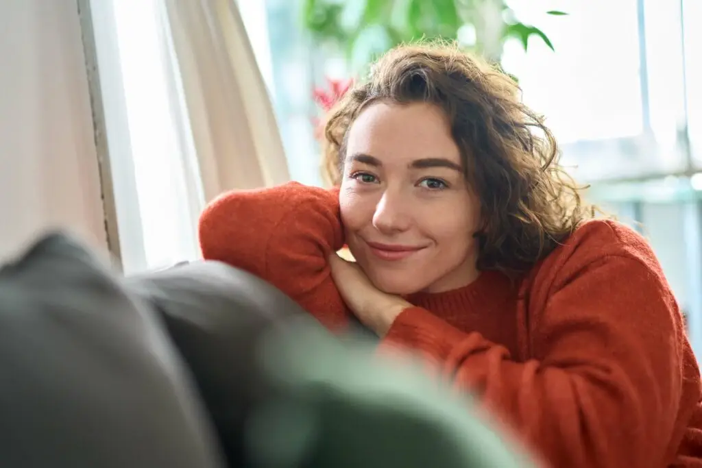 A young woman cozied on her couch, resting her head on her arm as it is propped up on the back cushion. She is happy to hear about the treatment options for separation anxiety disorder.