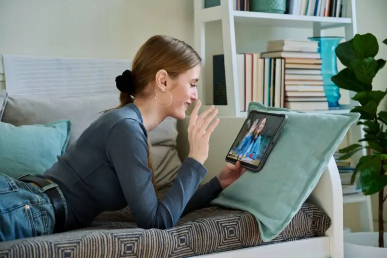 Young woman laying on her stomach, perched up on her arms, holding her tablet while she happily has her online ADHD therapy with her Makin Wellness therapist.