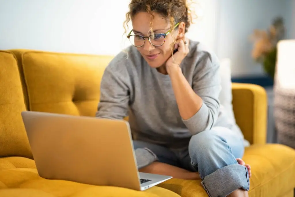 Middle-aged woman sitting on her yellow couch, researching the different types of ADHD on her laptop.