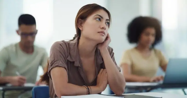 Young woman in a class feeling distracted, looking off to the side while her classmates are focused on their computers doing work.