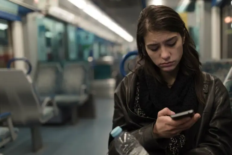 Young woman riding a bus at night is scrolling through social media on her phone looking depressed from what she sees.