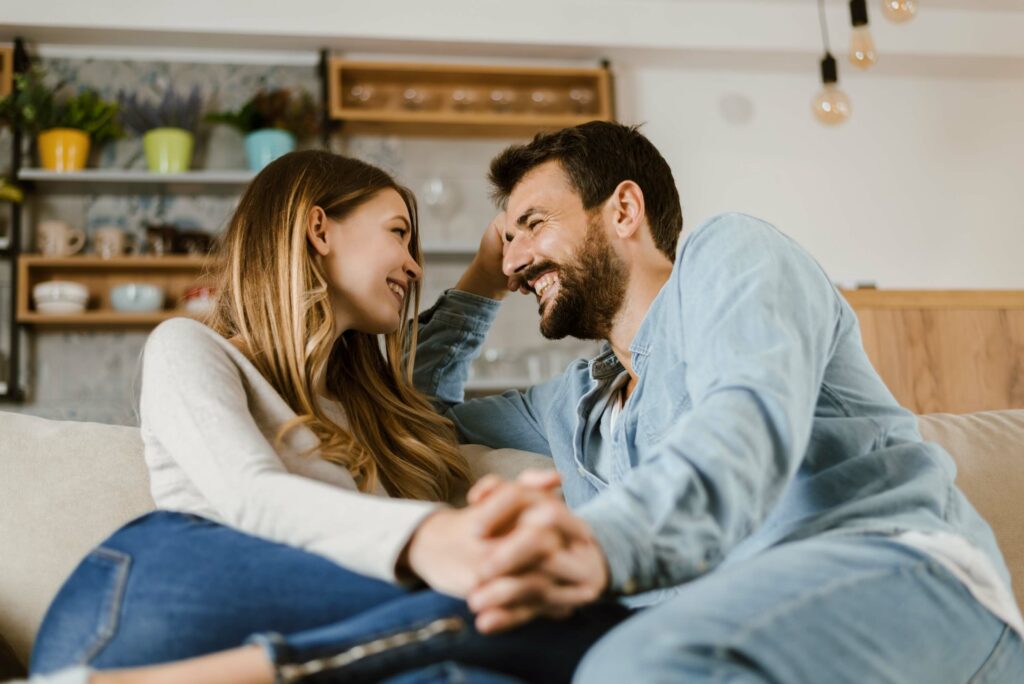 A loving young couple sitting on a couch, talking happily about their days as they hold hands.