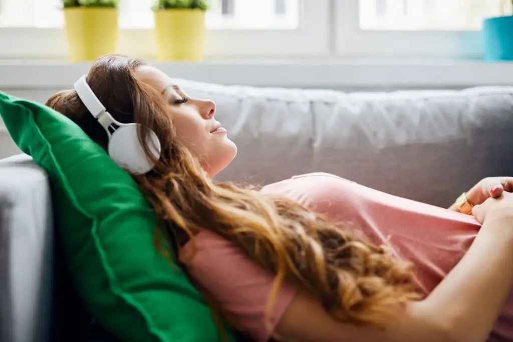 A young brunette woman laying on her back, head resting on a pillow, relaxing by knowing how to use progressive muscle relaxation.