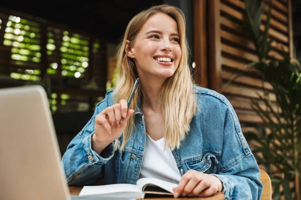 Young blond woman in a jean jacket, writing in a notebook on her desk, happy to write down the basics of her mindfulness practice.