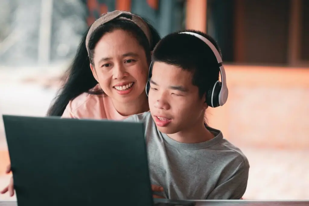 a young boy and his mother watching something on a laptop while the son wears headphones to protect him from overstimulation.