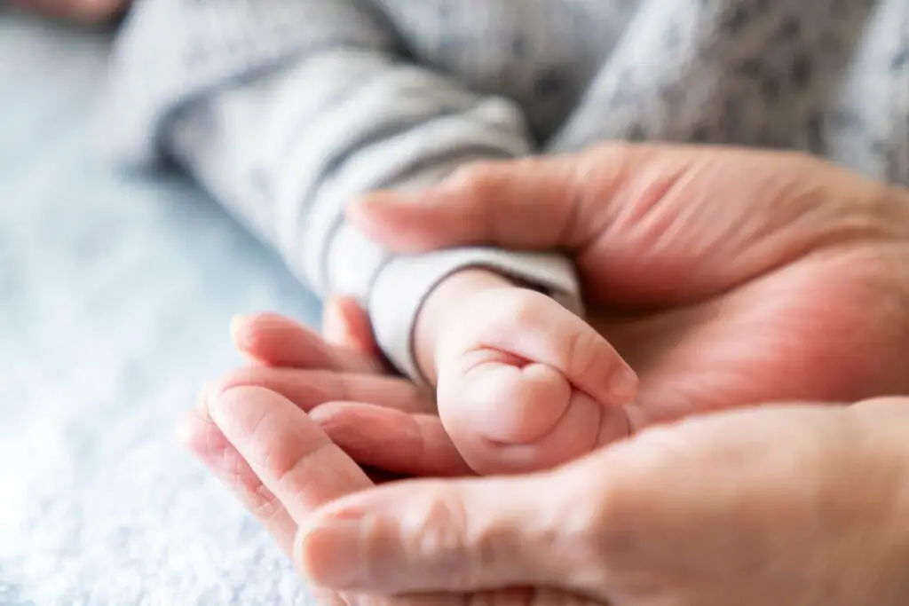 A mother holding her baby's hand and stretching their arm gently.