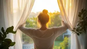 A young woman opening the curtains to see the morning sun.