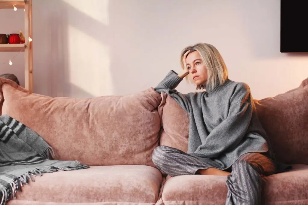 A young woman sitting on her couch with her head in her hands.