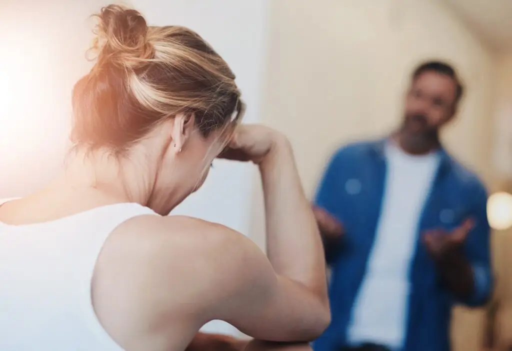 Middle aged blonde woman with her hand across her forehead, looking down as her partner says things to gaslight her.