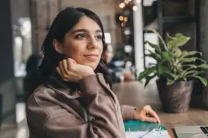 A young brunette woman staring out of her window feeling confident in setting boundaries with her partner.