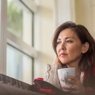 Middle aged woman holding a cup of tea looking out of her window thinking about losing a loved one