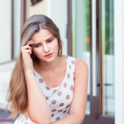 A young woman sitting outside with her head in her hand, coping with depression during college summer break