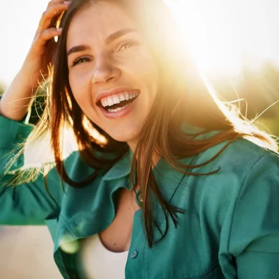 A young woman smiling and laughing while the sun is beaming behind her.