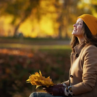 A middle-aged woman sitting on a park bench with fall leaves in her hand, thinking about how to move on after a divorce.